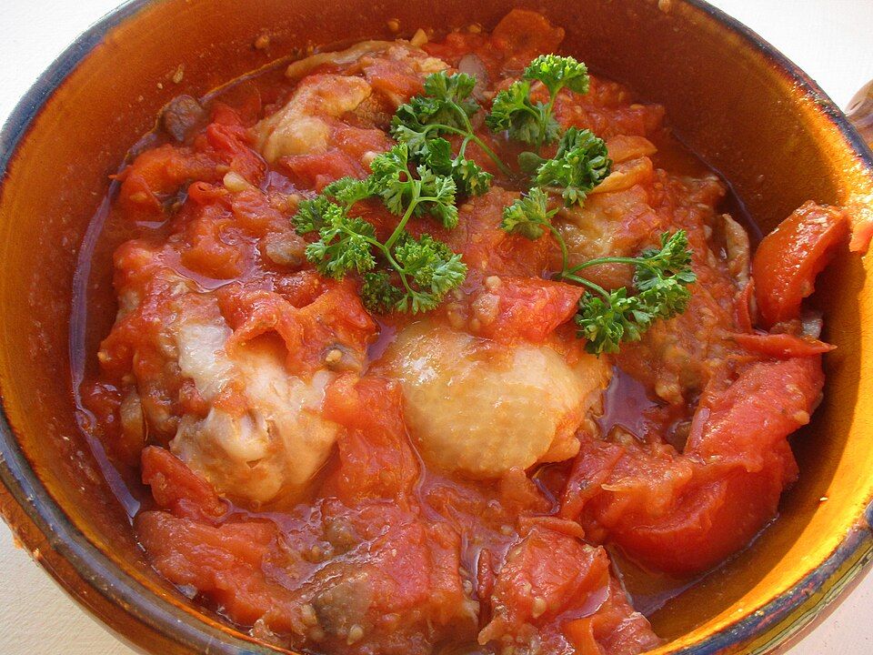 Poulet Marengo: chicken pieces in a rich tomato sauce, topped with fresh parsley, in an earthenware dish